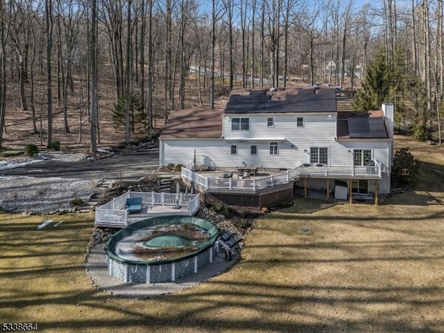 rear view of house with a yard, a wooden deck, and a view of trees