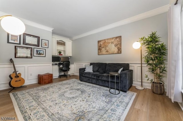 living room featuring a decorative wall, ornamental molding, wainscoting, light wood-type flooring, and built in desk