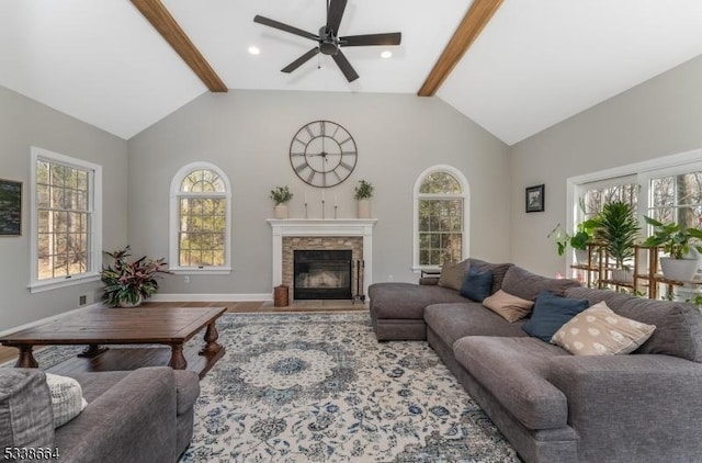 living area with vaulted ceiling with beams, wood finished floors, a glass covered fireplace, and baseboards