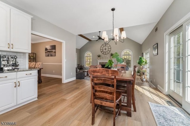 dining space with baseboards, visible vents, vaulted ceiling, light wood-style floors, and a fireplace