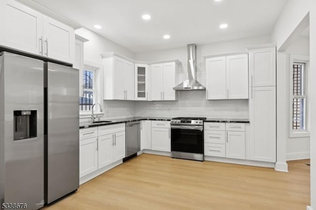 kitchen featuring a sink, dark countertops, stainless steel appliances, wall chimney exhaust hood, and light wood finished floors