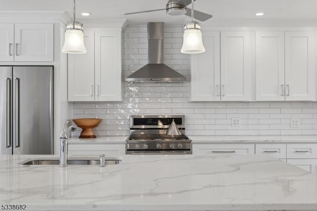 kitchen featuring white cabinets, stainless steel appliances, hanging light fixtures, and wall chimney range hood