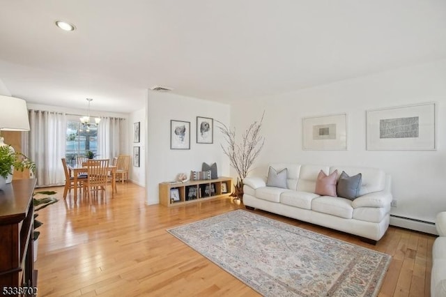 living room featuring a baseboard heating unit, light wood-type flooring, a chandelier, and visible vents