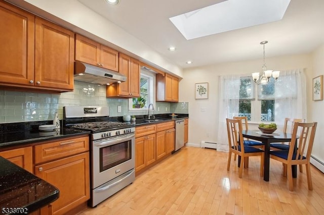 kitchen with brown cabinets, light wood finished floors, tasteful backsplash, appliances with stainless steel finishes, and under cabinet range hood