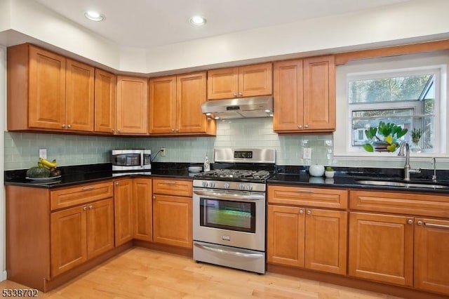 kitchen with brown cabinets, stainless steel appliances, light wood-type flooring, under cabinet range hood, and a sink