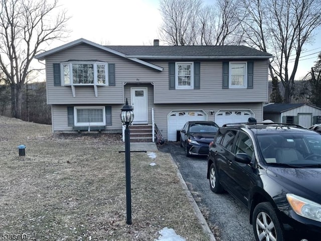 raised ranch with an attached garage, driveway, and a shingled roof