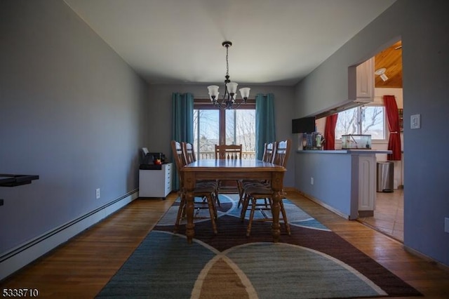 dining room with a notable chandelier, wood finished floors, baseboard heating, and a healthy amount of sunlight