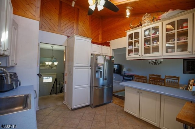 kitchen with high vaulted ceiling, white cabinetry, stainless steel fridge, light tile patterned floors, and glass insert cabinets