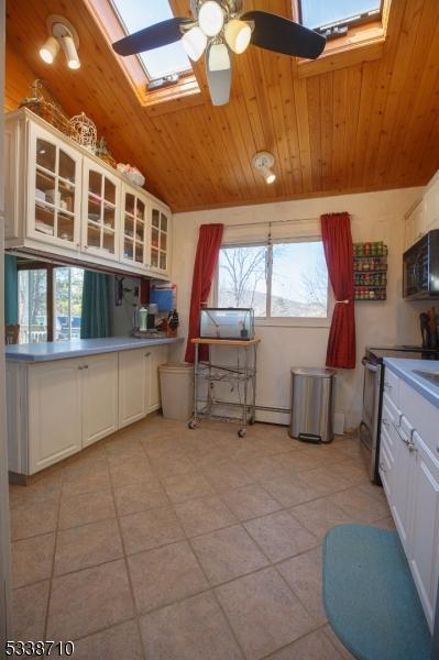 kitchen with glass insert cabinets, black microwave, wood ceiling, vaulted ceiling with skylight, and stainless steel range with electric cooktop