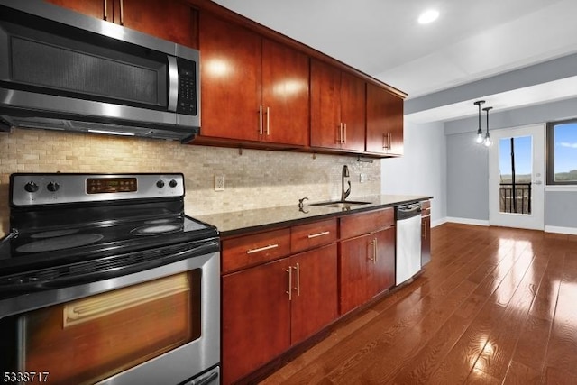 kitchen featuring dark wood-type flooring, sink, hanging light fixtures, stainless steel appliances, and backsplash