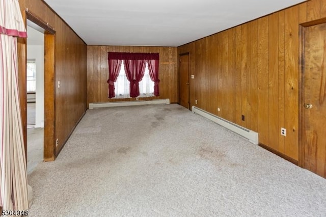 empty room with a baseboard radiator, light carpet, and wood walls