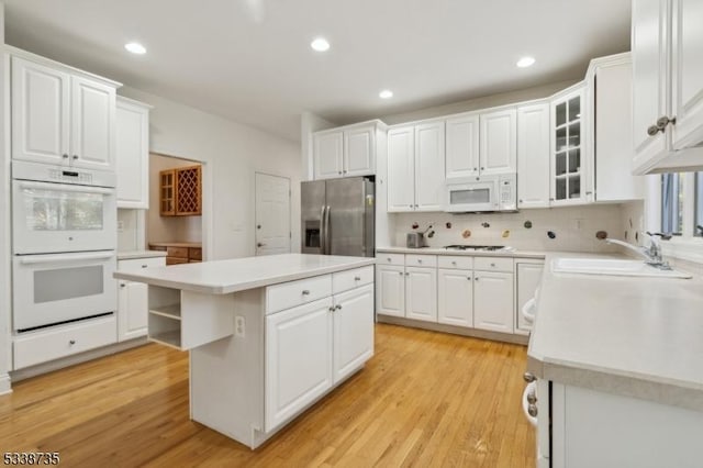 kitchen with white appliances, sink, light wood-type flooring, a kitchen island, and white cabinets