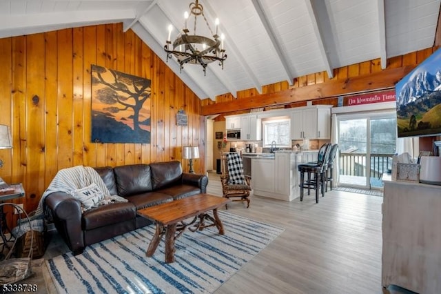 living area featuring light wood finished floors, wooden walls, beamed ceiling, high vaulted ceiling, and a notable chandelier