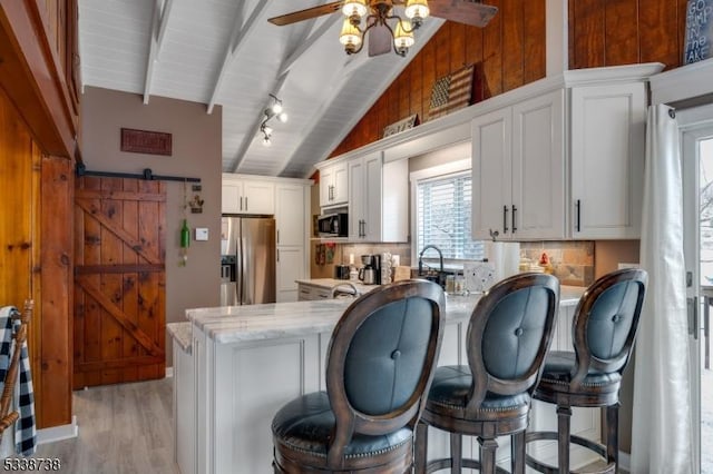 kitchen featuring lofted ceiling with beams, a barn door, stainless steel appliances, a peninsula, and light wood-style floors