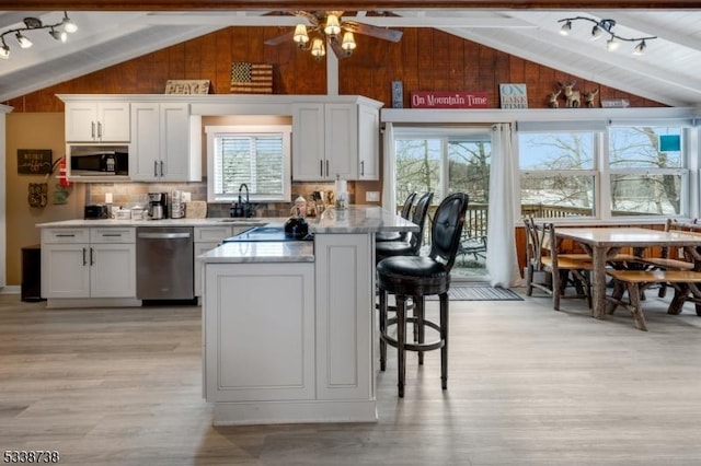 kitchen featuring lofted ceiling with beams, light wood-style flooring, wooden walls, and stainless steel appliances