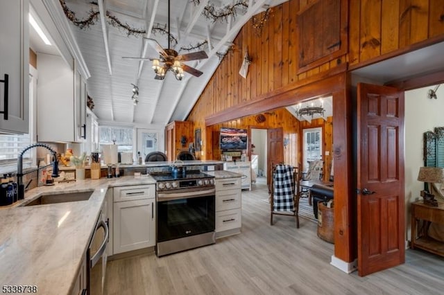 kitchen featuring light wood-style flooring, wooden walls, a peninsula, a sink, and appliances with stainless steel finishes