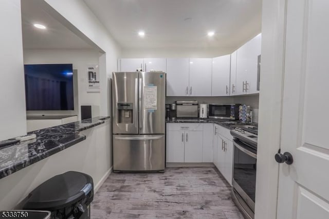 kitchen featuring light wood-style flooring, appliances with stainless steel finishes, white cabinets, and dark stone counters