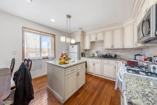 kitchen featuring a kitchen island, decorative light fixtures, hardwood / wood-style flooring, light stone counters, and white appliances