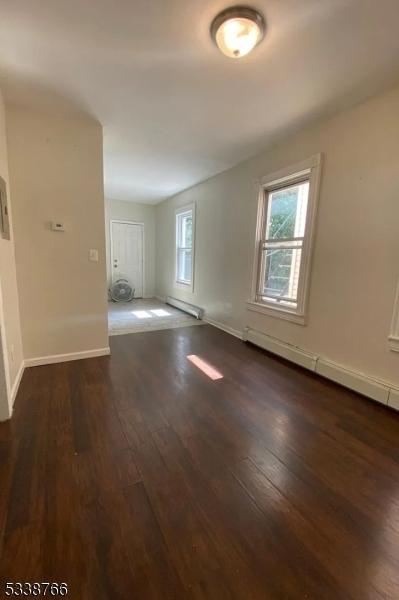 unfurnished room with a baseboard heating unit, dark hardwood / wood-style floors, and plenty of natural light