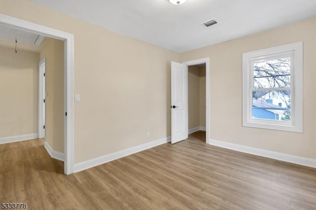 unfurnished bedroom featuring baseboards, light wood-style flooring, visible vents, and attic access