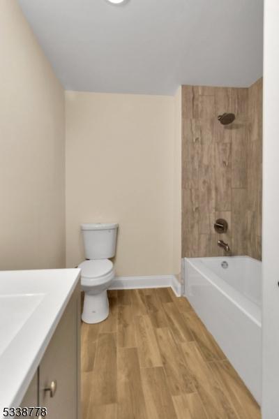 bathroom with shower / washtub combination, toilet, vanity, wood finished floors, and baseboards