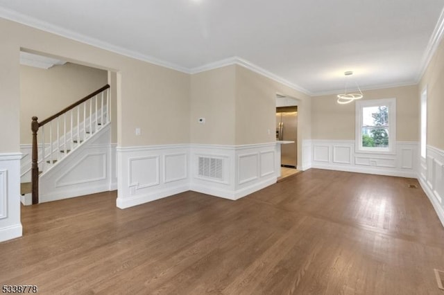 spare room featuring ornamental molding, wood finished floors, visible vents, and stairs