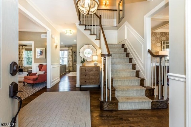 foyer with crown molding, visible vents, a decorative wall, dark wood-type flooring, and wainscoting