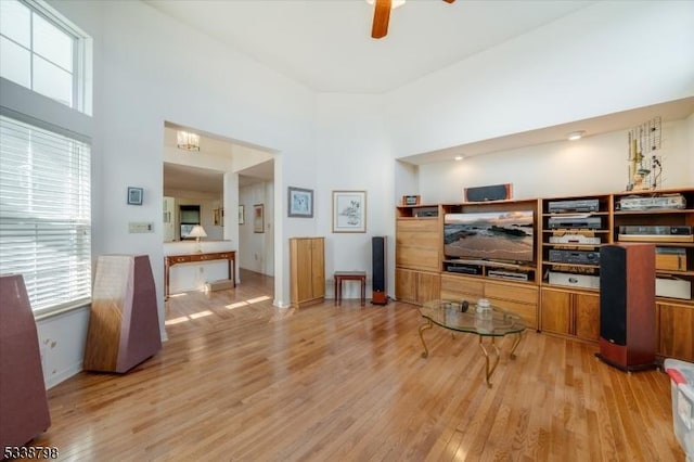 living room with a high ceiling, wood finished floors, a ceiling fan, and a healthy amount of sunlight