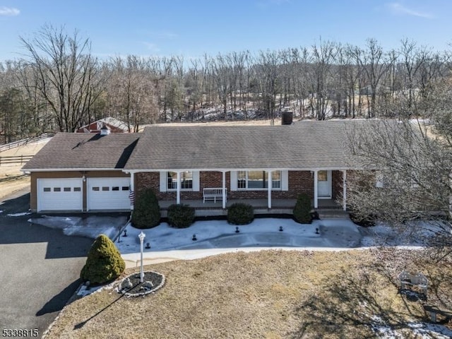 ranch-style house with a garage, brick siding, driveway, and roof with shingles