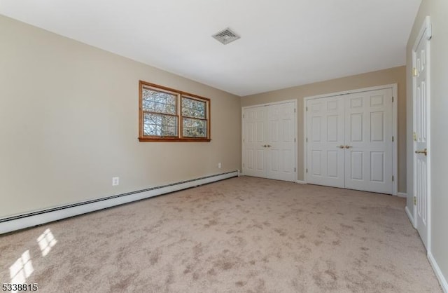 unfurnished bedroom featuring two closets, visible vents, a baseboard heating unit, light carpet, and baseboards