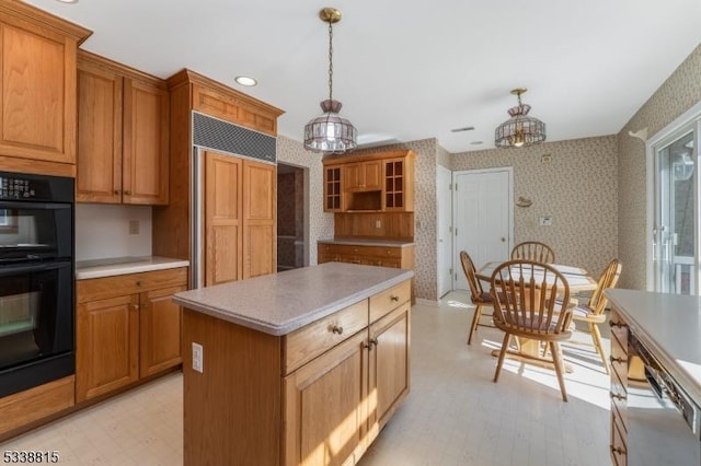 kitchen with wallpapered walls, dobule oven black, a kitchen island, light countertops, and pendant lighting