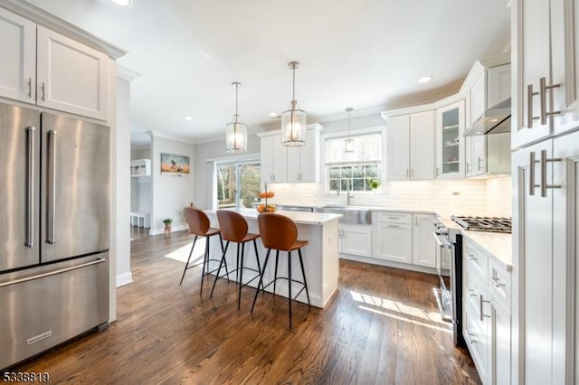 kitchen with hanging light fixtures, stainless steel appliances, a breakfast bar, a center island, and white cabinetry