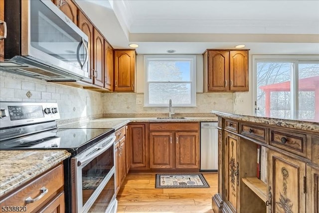 kitchen featuring light stone counters, brown cabinets, stainless steel appliances, crown molding, and a sink