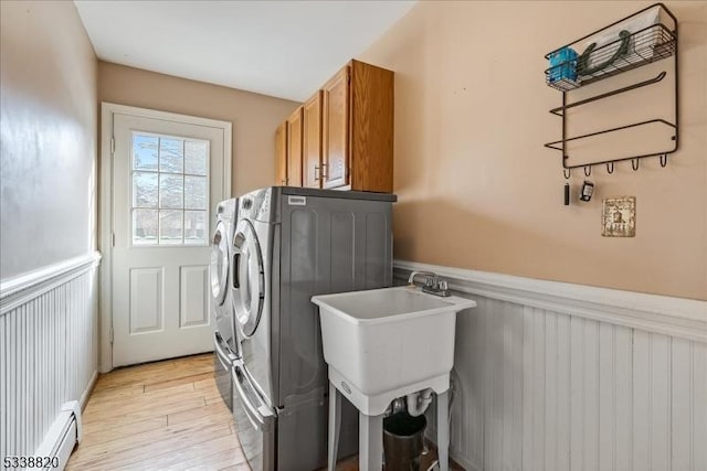 washroom with a wainscoted wall, baseboard heating, light wood-type flooring, independent washer and dryer, and cabinet space