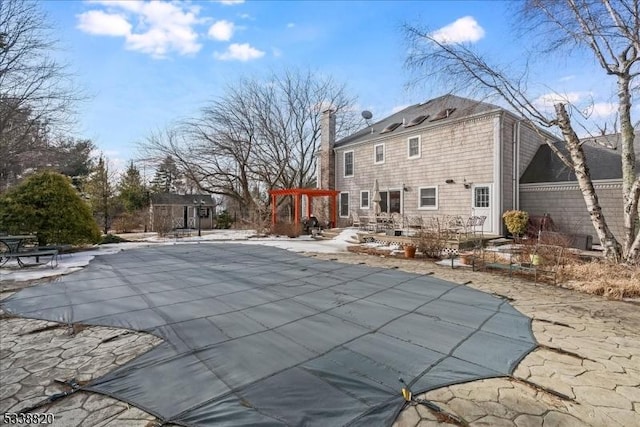 rear view of property with a covered pool, a patio, a chimney, and an outdoor structure