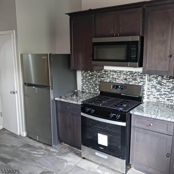 kitchen with light stone countertops, tasteful backsplash, appliances with stainless steel finishes, and dark brown cabinets