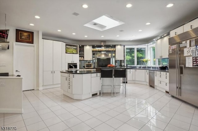 kitchen with stainless steel appliances, dark countertops, a kitchen island, and white cabinetry