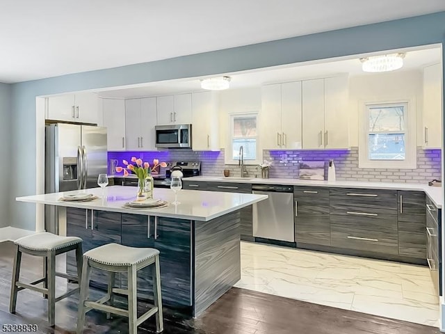 kitchen with a breakfast bar area, stainless steel appliances, white cabinets, a center island, and sink