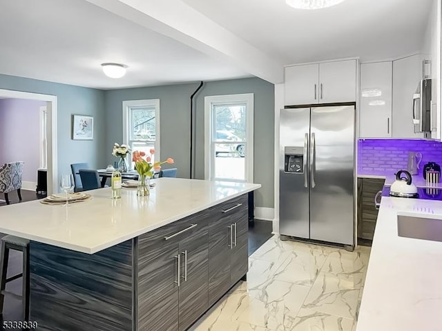 kitchen with tasteful backsplash, stainless steel appliances, a kitchen island, white cabinetry, and a kitchen bar