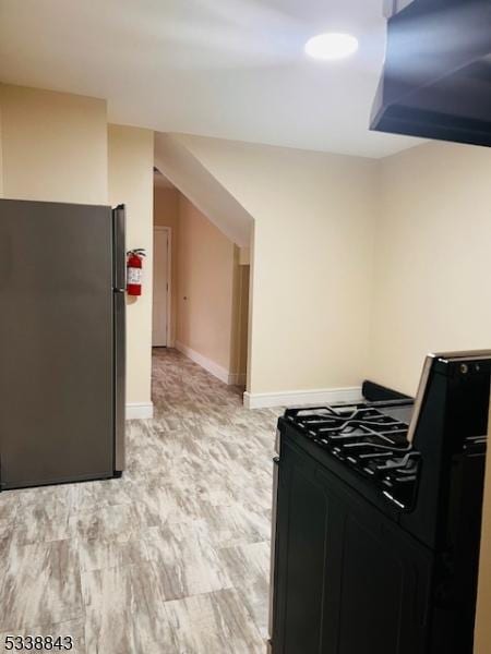 kitchen featuring gas range oven, light wood-type flooring, freestanding refrigerator, and baseboards