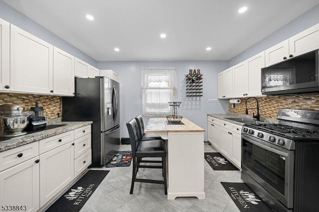 kitchen with light stone counters, stainless steel appliances, a sink, white cabinetry, and a center island