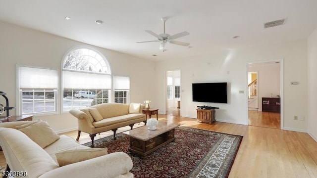 living area with visible vents, light wood-type flooring, a ceiling fan, and baseboards