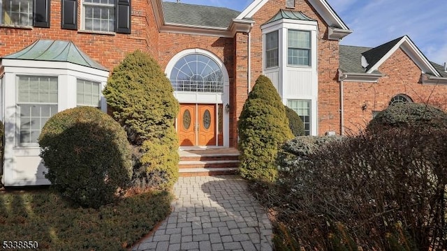 entrance to property featuring roof with shingles and brick siding