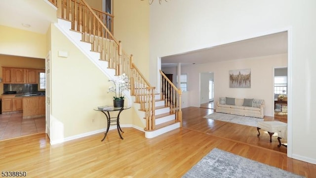 foyer entrance featuring a high ceiling, stairway, light wood-type flooring, and baseboards