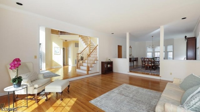 living area with a notable chandelier, stairway, light wood-style flooring, and crown molding