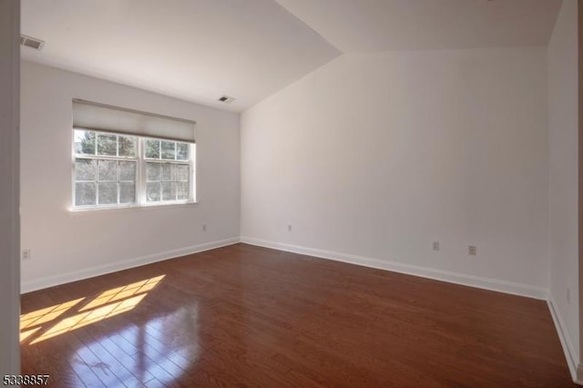 unfurnished room featuring dark wood-style floors, baseboards, visible vents, and vaulted ceiling