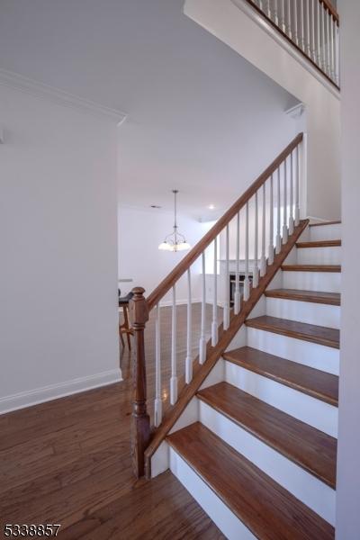 stairs with an inviting chandelier, baseboards, ornamental molding, and wood finished floors