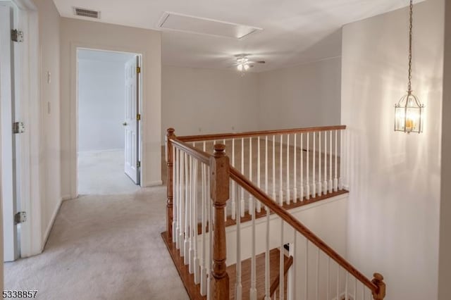 hallway featuring attic access, visible vents, light colored carpet, and an upstairs landing