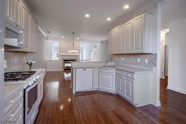 kitchen with light countertops, dark wood-type flooring, a sink, white appliances, and a peninsula