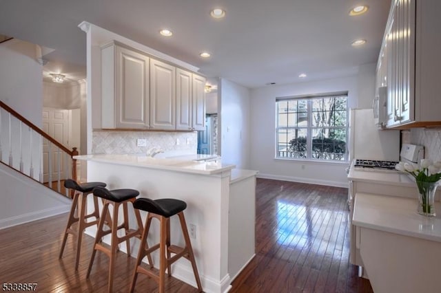 kitchen with tasteful backsplash, light countertops, dark wood finished floors, and a kitchen bar